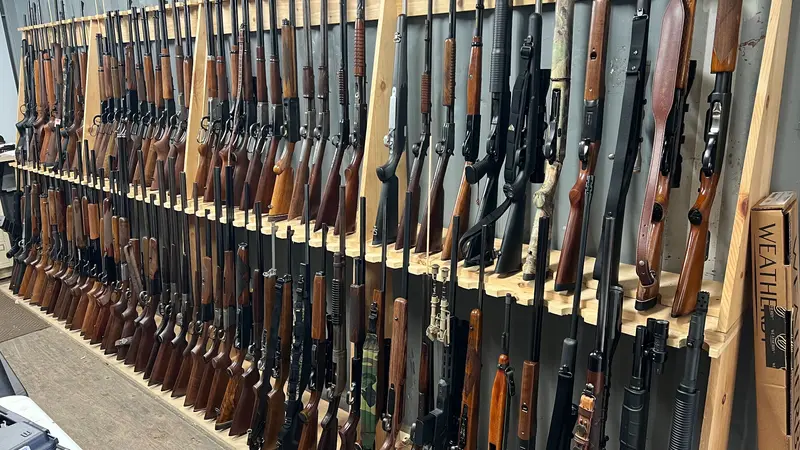 A long wall rack of rifles and shotguns with wooden stocks in a gun shop